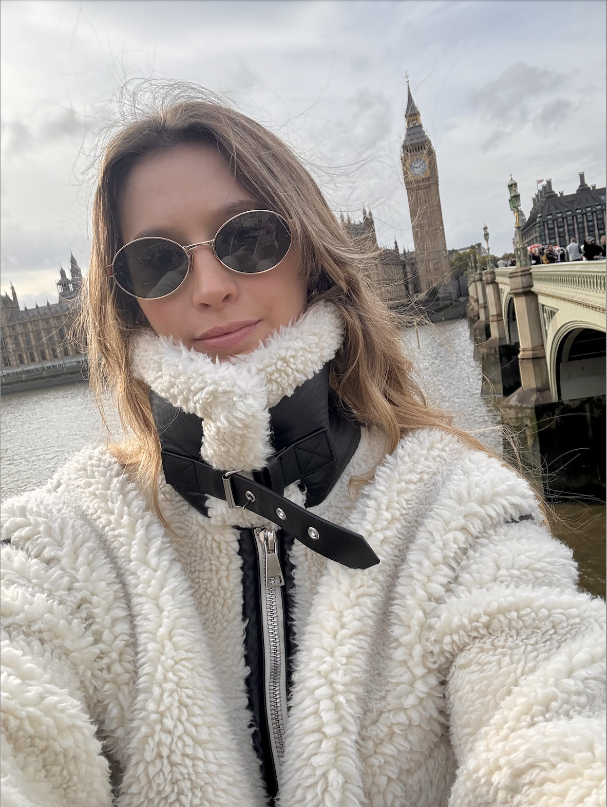Ailen Zygier in London with Big Ben in the background, wearing sunglasses and white fleece jacket, demonstrating international experience in English-speaking countries